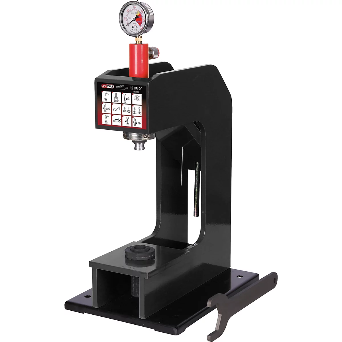 Schwarze Hydraulikpresse mit Manometer und rotem Ventil. Auf einer schwarzen Grundplatte liegt ein Schraubenschlüssel.